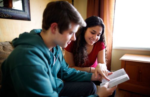 young woman pointing to a page in a book held by a young man