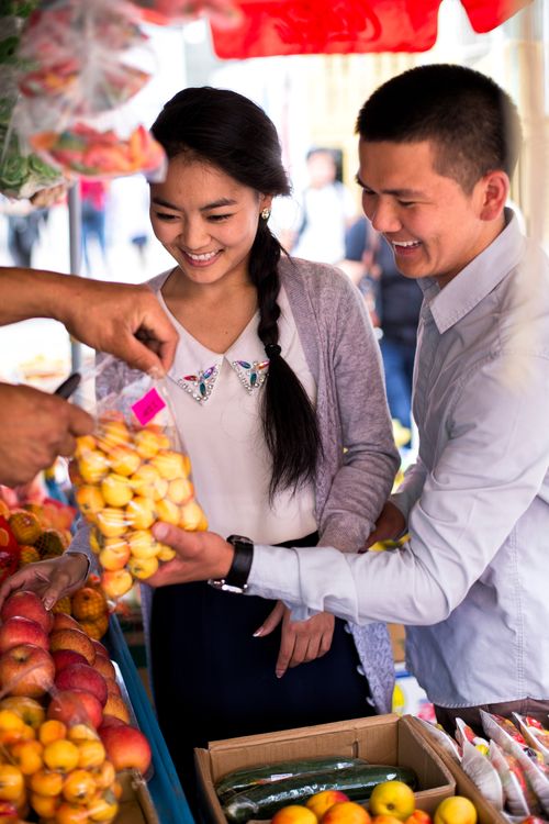 A woman with black hair in a braid and a man in a light blue button-up shirt shopping for fruit in a local Mongolian market.