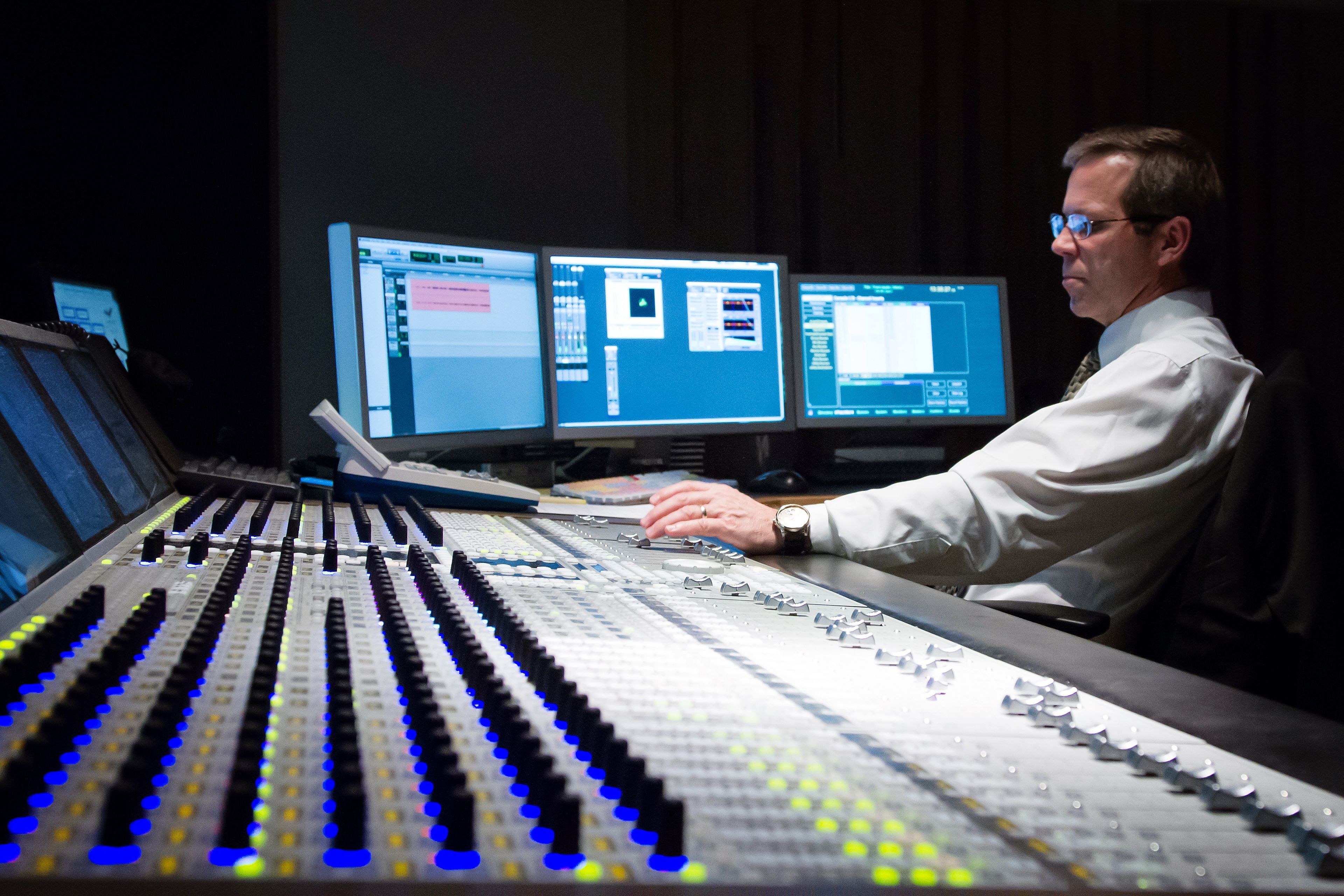 A man sits at a soundboard and adjusts it.  