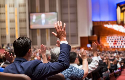 man in Conference Center raising right arm for sustaining vote