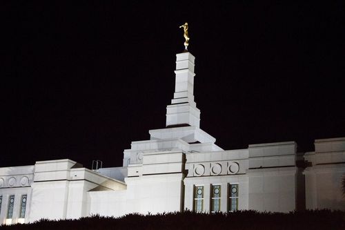 The spire and angel Moroni on top of the Porto Alegre Brazil Temple, lit up against a dark night sky.
