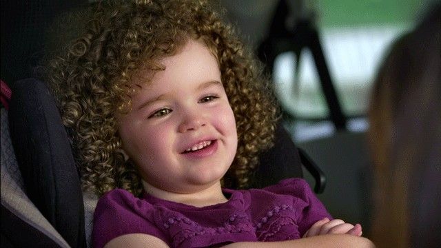 A young girl smiles as her grandmother puts her in a car seat