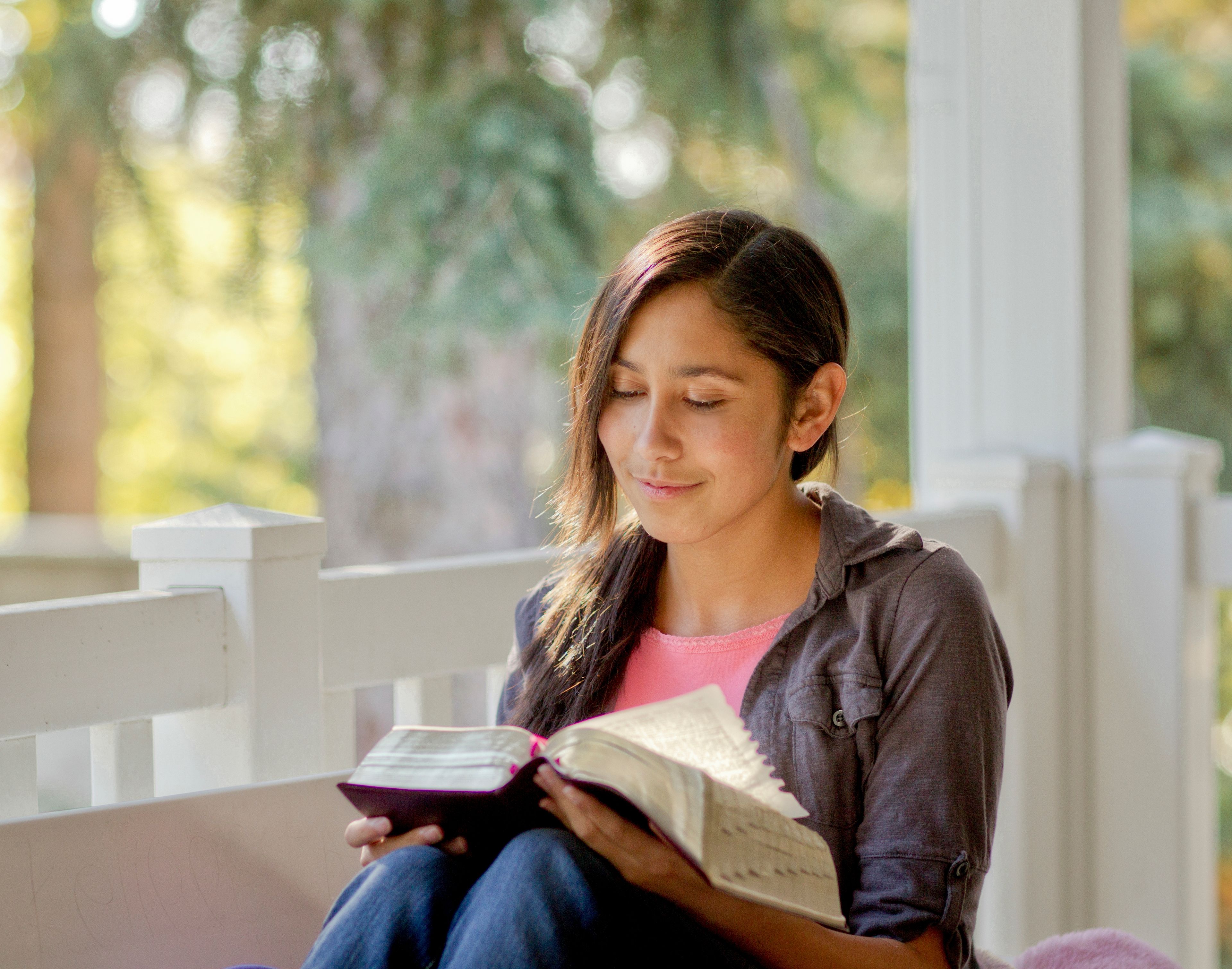 A young woman sits on a porch and reads her scriptures.  