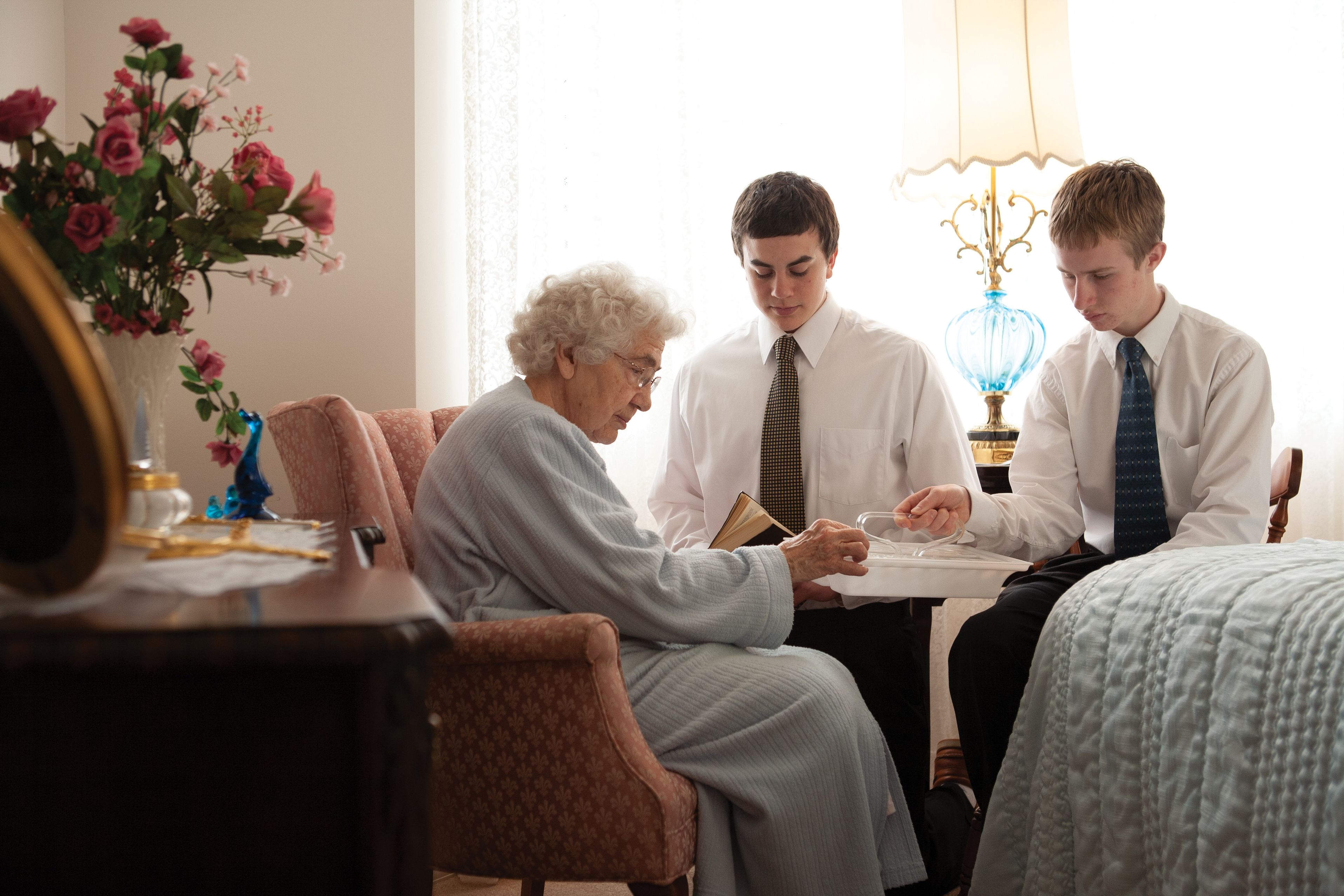 Two young men administering the sacrament to an elderly woman in her home.