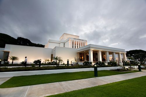 A wide-angle view of the front of the Laie Hawaii Temple in the evening, with the exterior lights turned on.