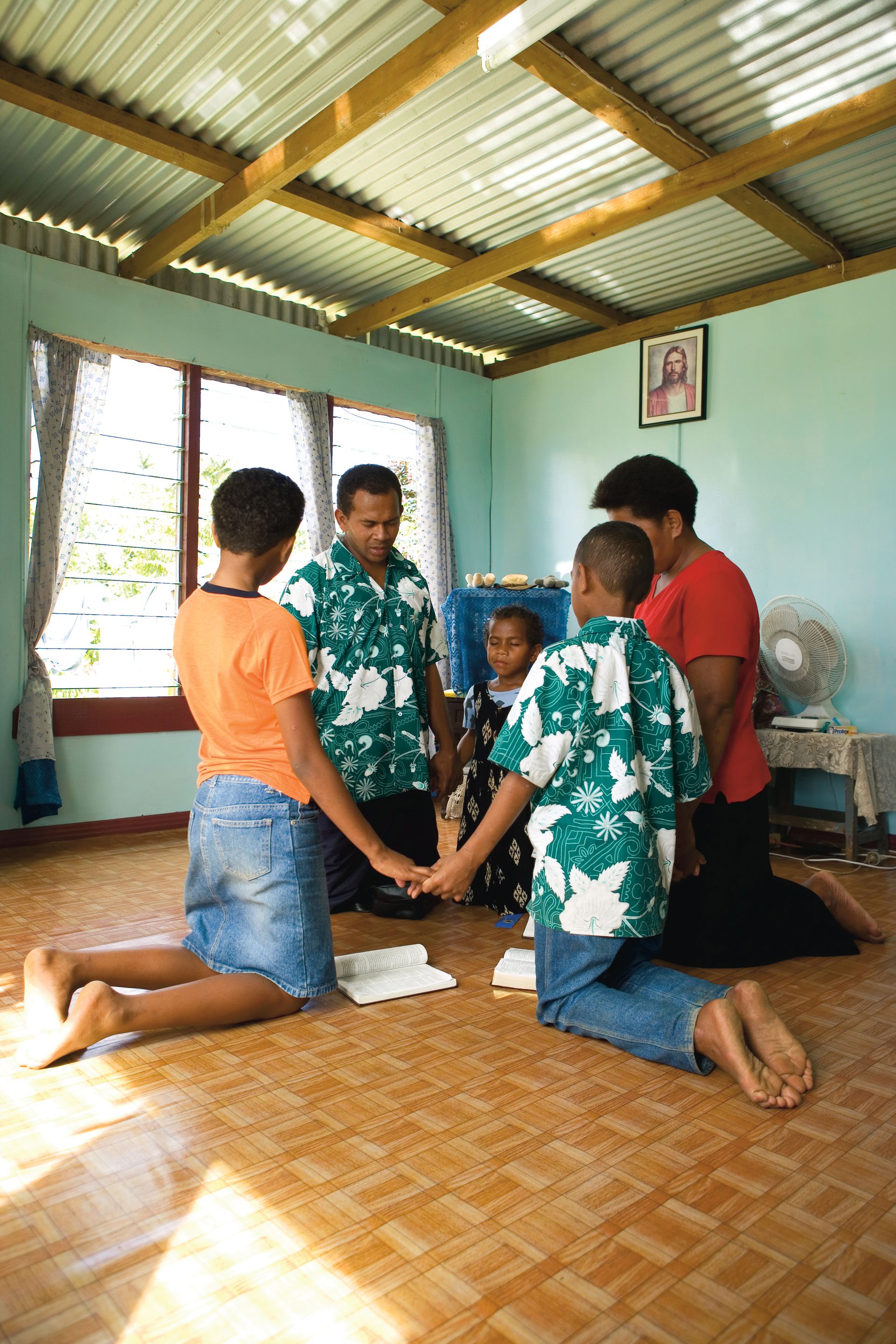 A family in Fiji holding hands and praying together.