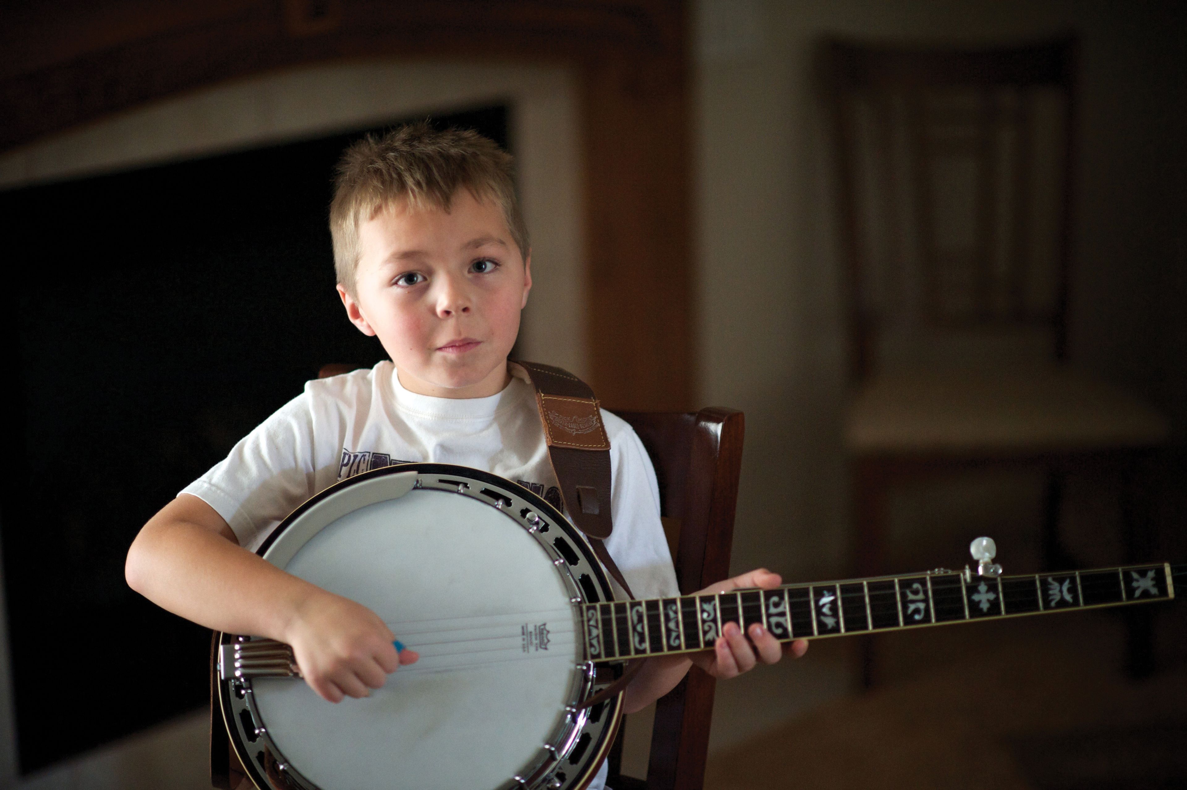 A boy sits down and plays a banjo.