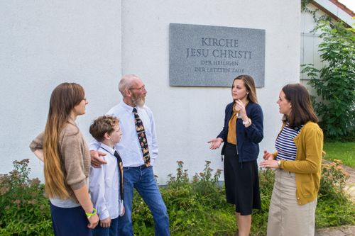 sister missionaries talking to a family in front of a Church building