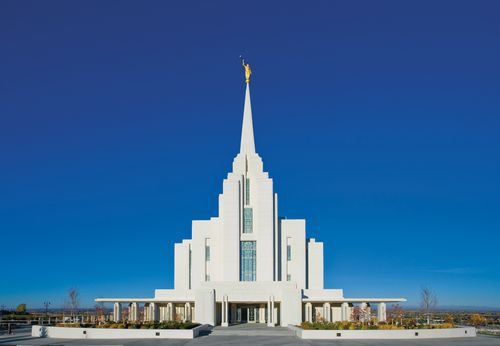 The front of the Rexburg Idaho Temple, including the entrance and grounds on either side, with a view of the valley in the background.