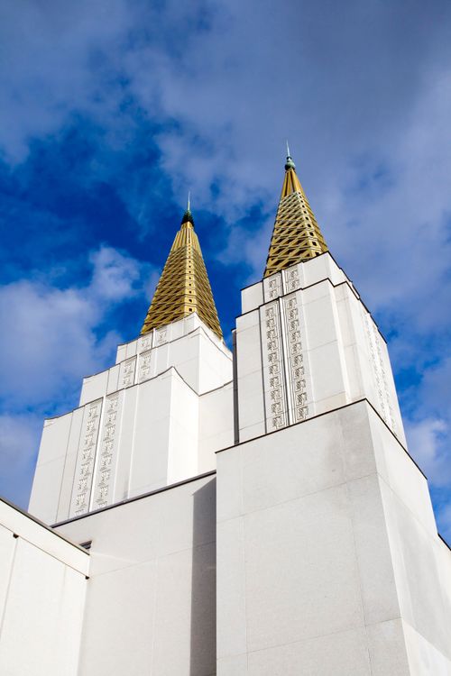 Two of the spires on top of the Oakland California Temple against a deep blue sky with thin white clouds.