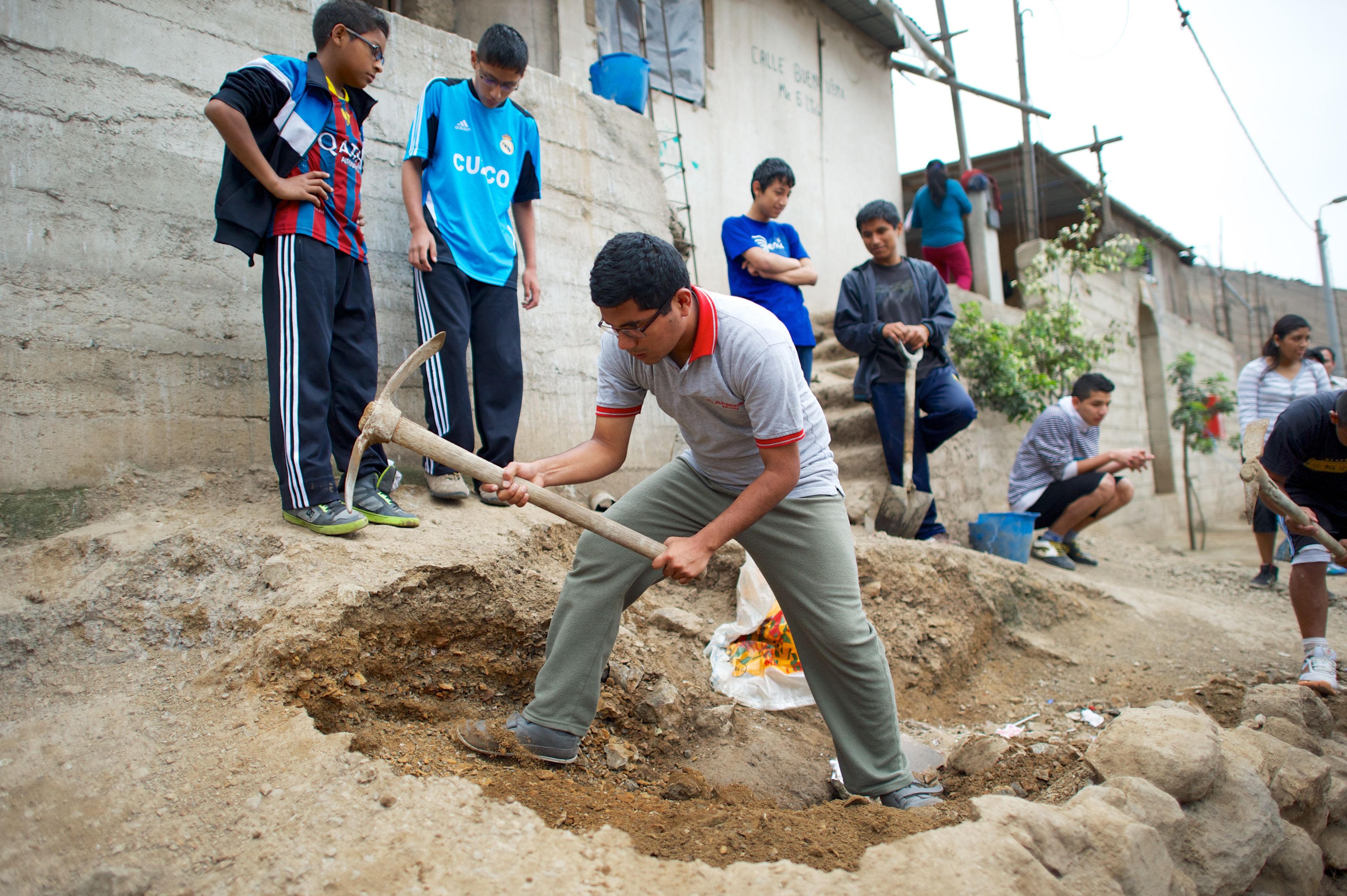 A young man uses a pickaxe to dig through dirt during a service activity in Peru.