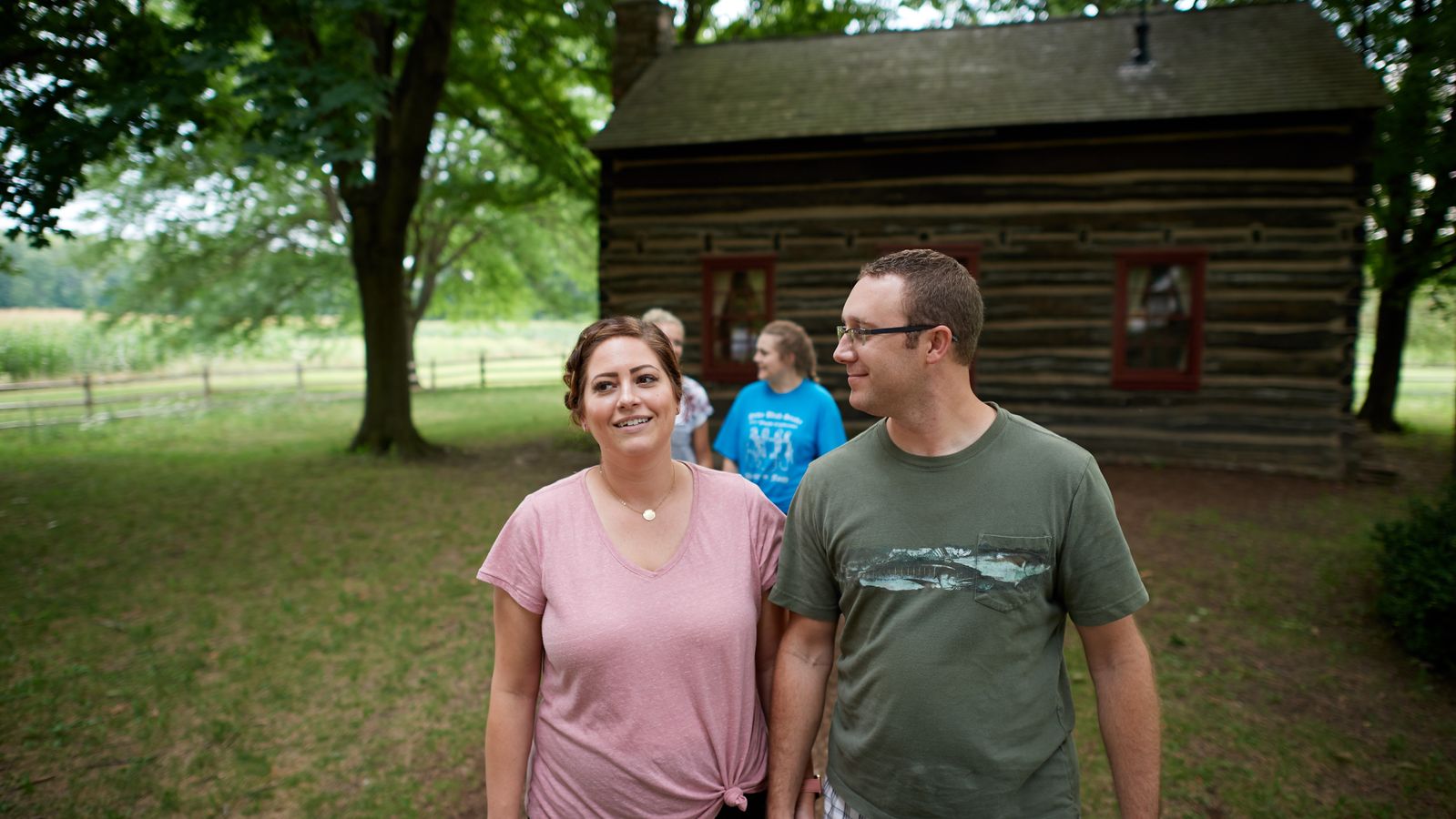 Exterior shots of the Peter and Mary Whitmer Farm. There is a log cabin with a red door. It is surrounded by trees.
Families walk and talk outside of the farm.