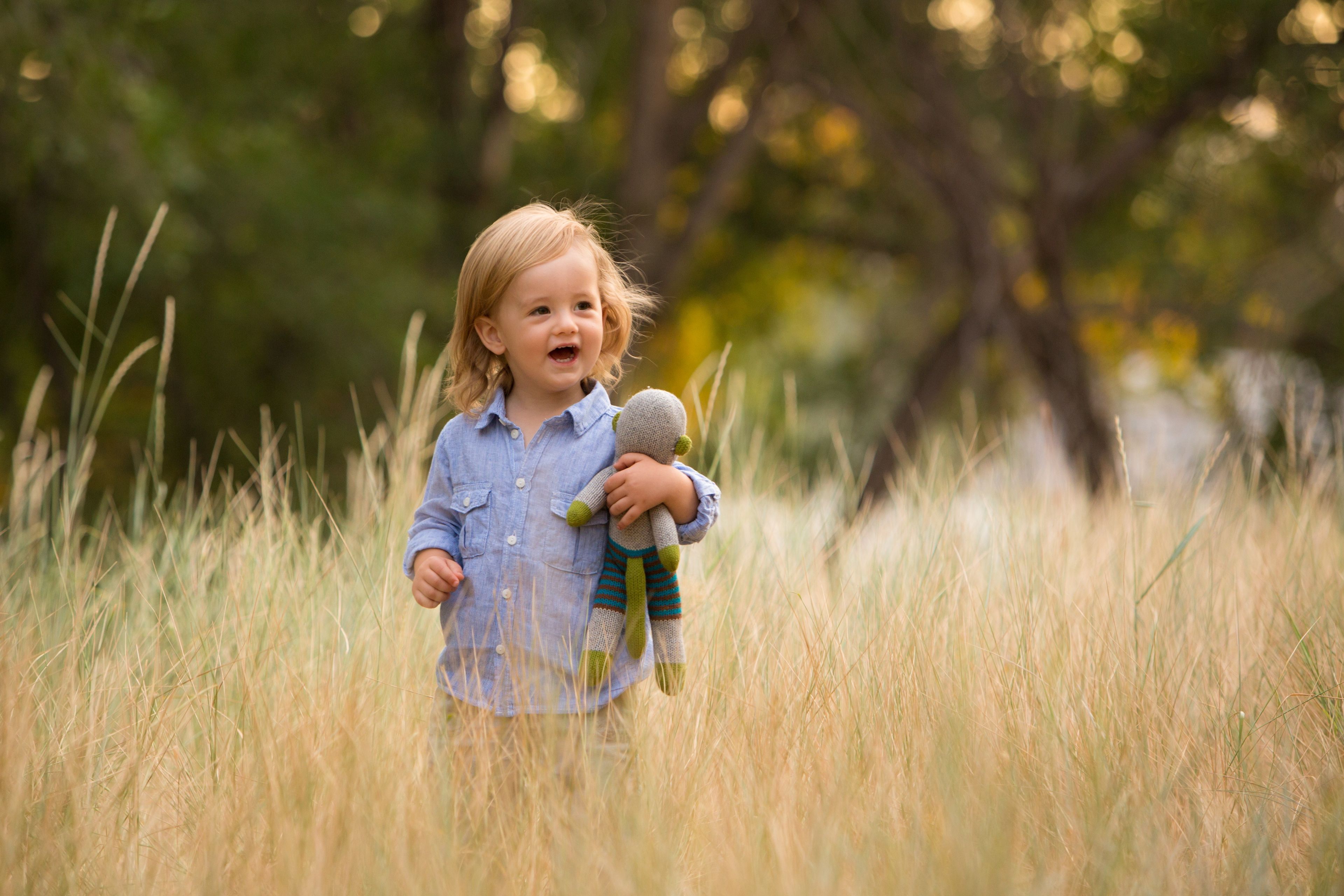 A toddler boy with a stuffed animal in a field.
