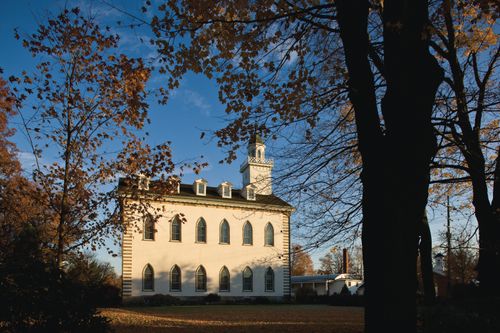 A view of the Kirtland Temple on an autumn day, with the trunk of a large tree partially blocking the view.