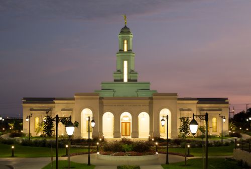 A front view of the Trujillo Peru Temple at dusk, with a purple sky overhead and a row of street lamps leading to the entrance.
