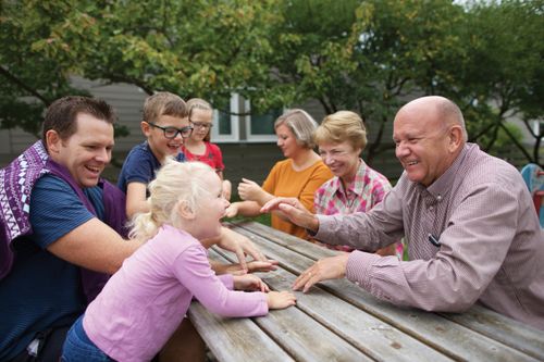 A family consisting of grandparents, parents, and children sitting outside at a wooden picnic table.