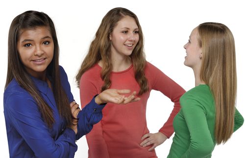 Three teenage girls standing together.  Two are talking while the other is looking away from them.