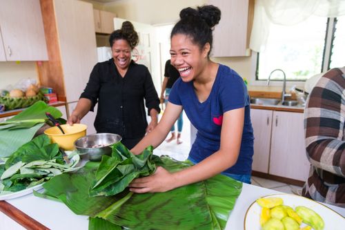 two laughing women working with banana leaves in a kitchen