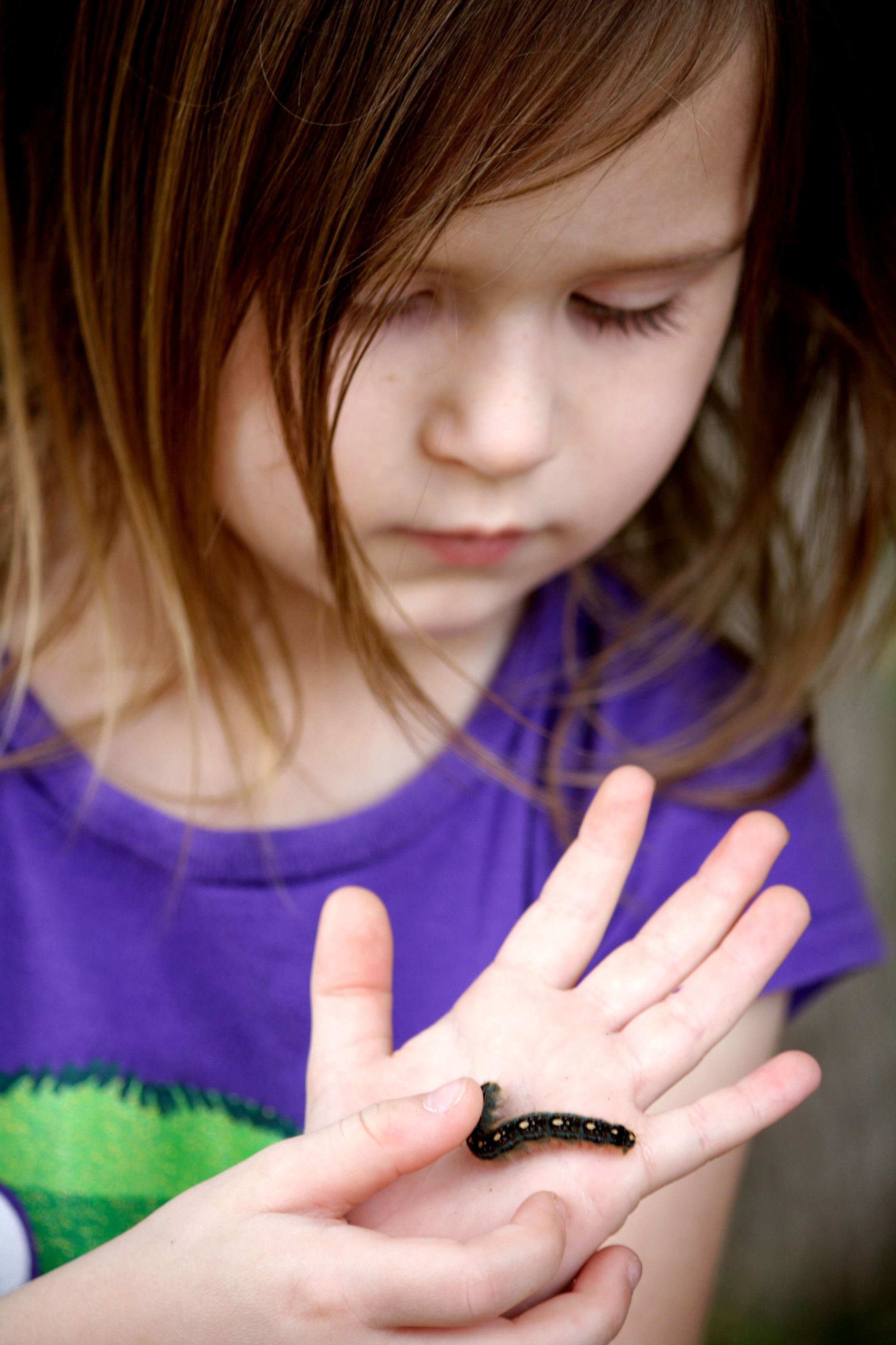 A young girl holds a caterpillar in her hand.