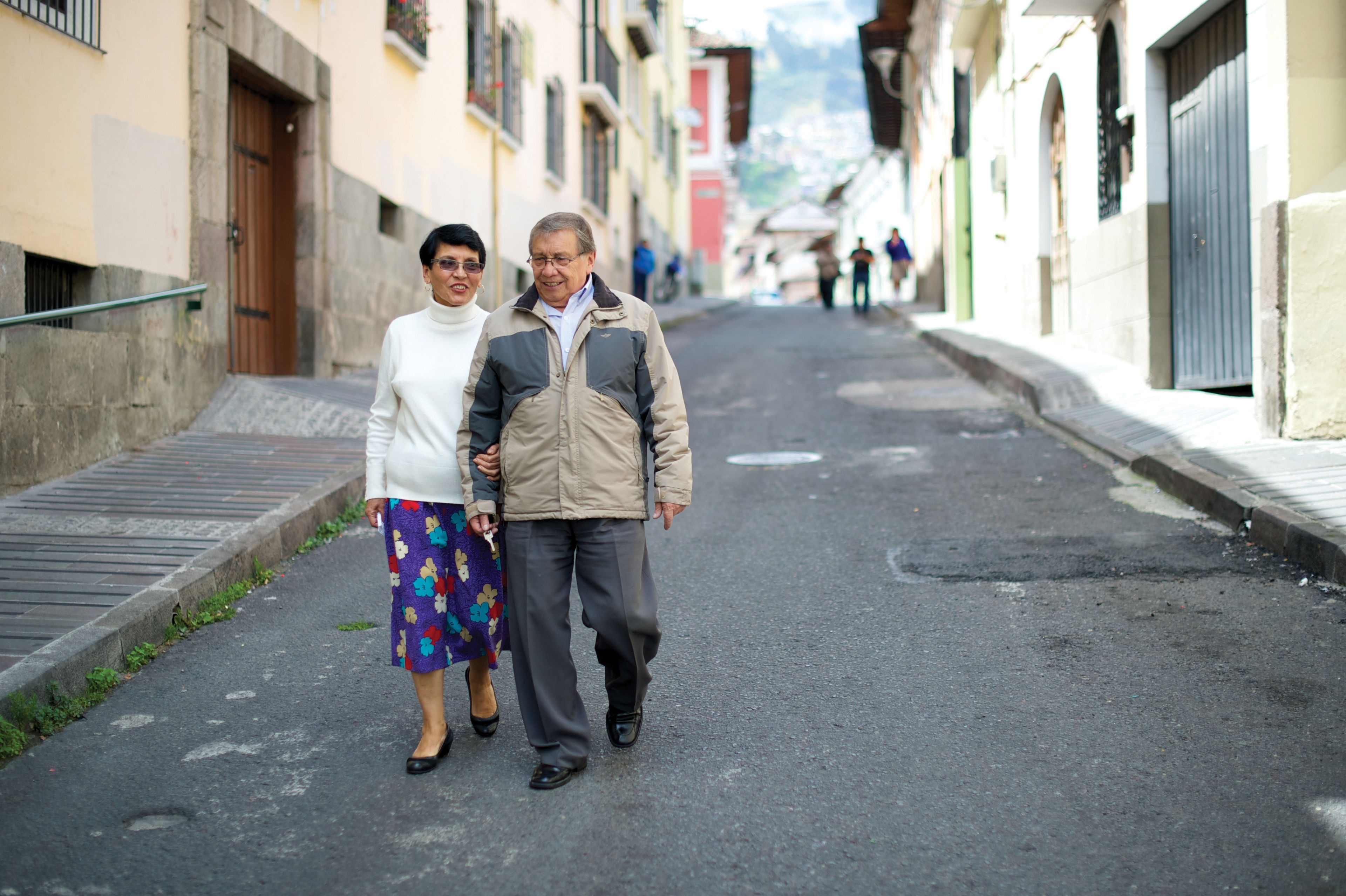 An elderly couple from Ecuador walking with linked arms down a street together.