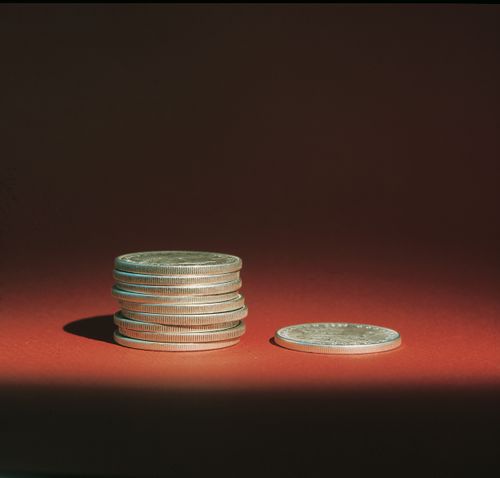 A stack of nine silver coins next to a single silver coin on a red background, with a single light source casting shadows.