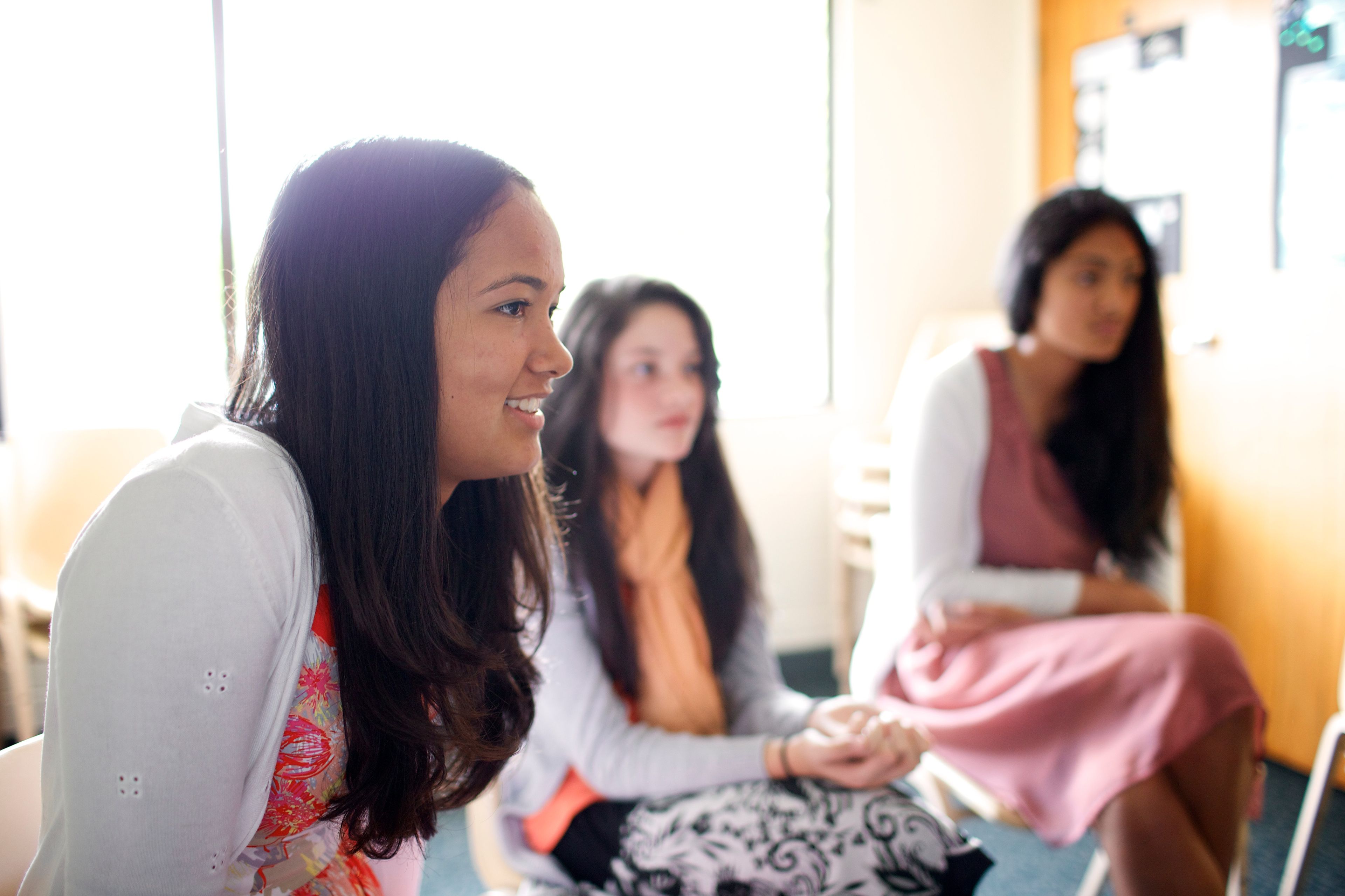 Three young women sit in a classroom during a Church meeting.