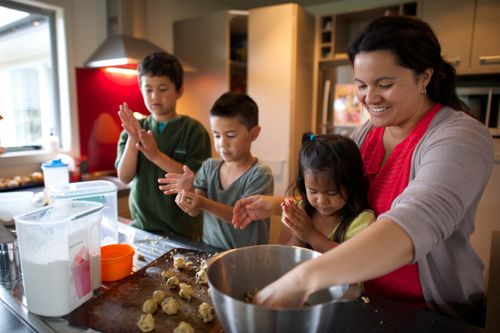 A mother bakes cookies with her three children in the kitchen.