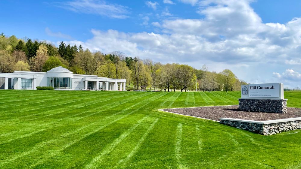 Large grey building with large green field and a sign reading “Hill Cumorah"