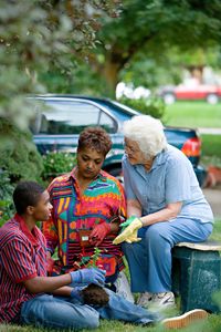 A young man and his mother working in a flower garden as an elderly woman looks on.