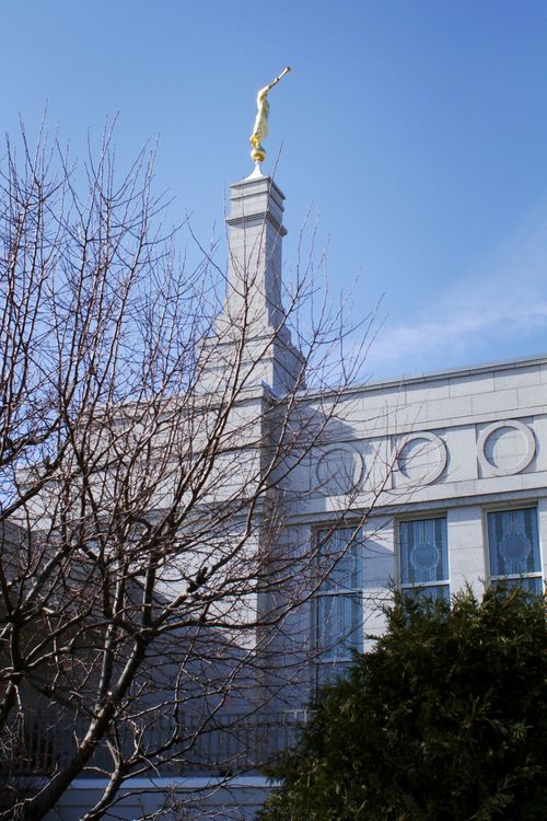 A partial view of the St. Paul Minnesota Temple through trees on the grounds, including a view of the spire.