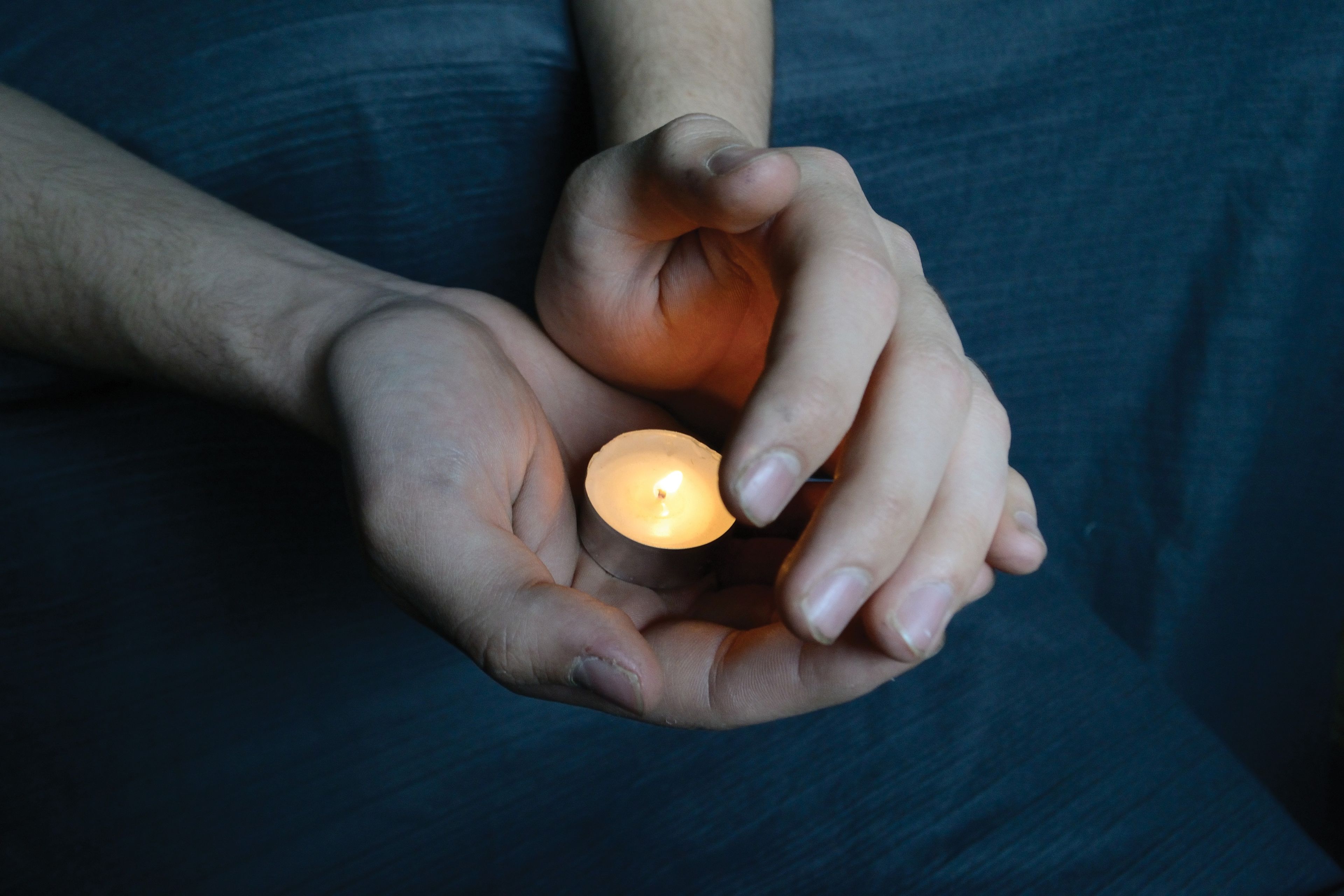 Hands holding a candle in the dark, sheltering the flame from the wind.