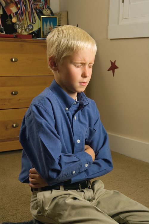 A young boy kneels down, folds his arms, and closes his eyes while saying a prayer in his bedroom.