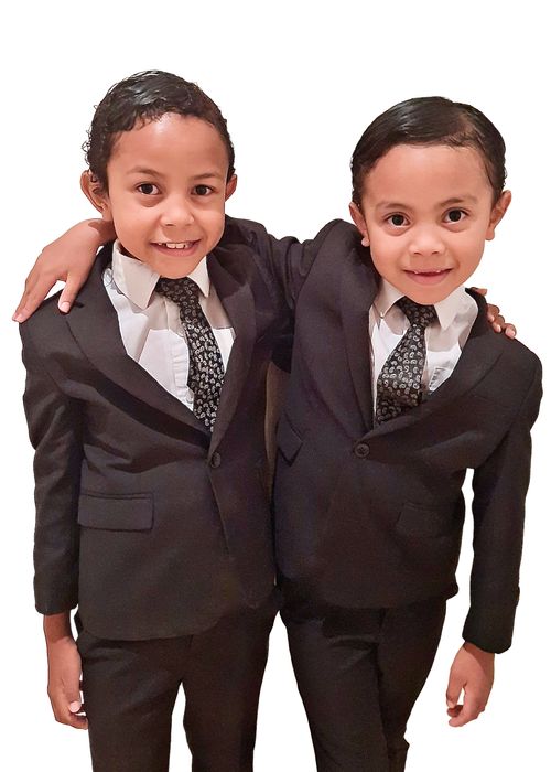 Two boys in dark suits standing next to each other arm in arm