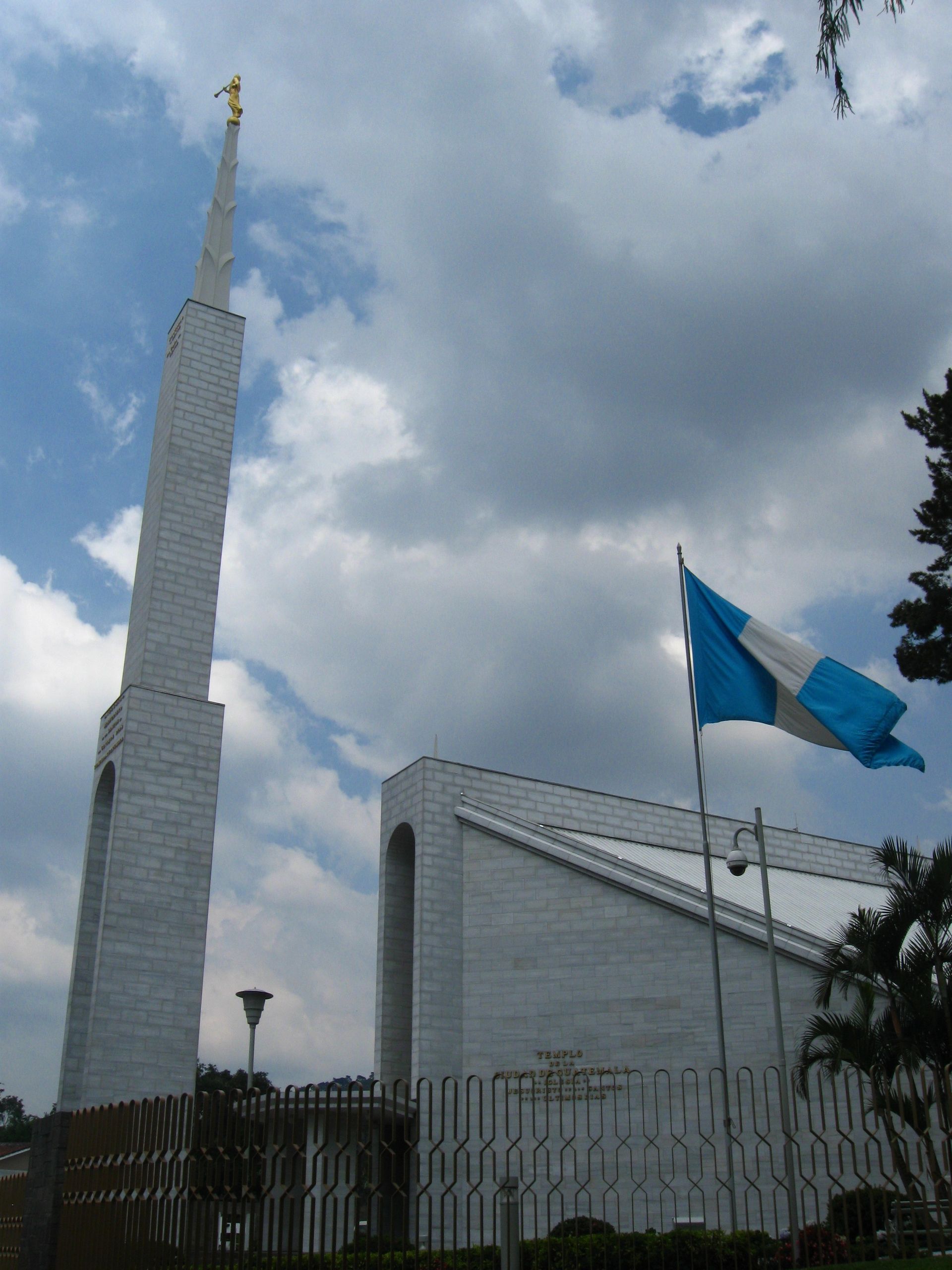 The Guatemala City Guatemala Temple side view, including the spire, flag, and gates.
