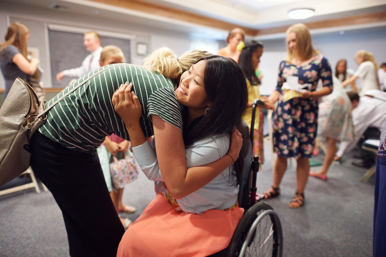 Una joven en silla de ruedas está hablando con otras mujeres jóvenes y recibe un abrazo