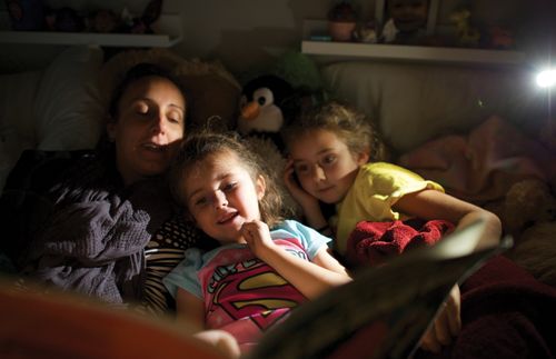 A mother reads with her daughters at night in bed.