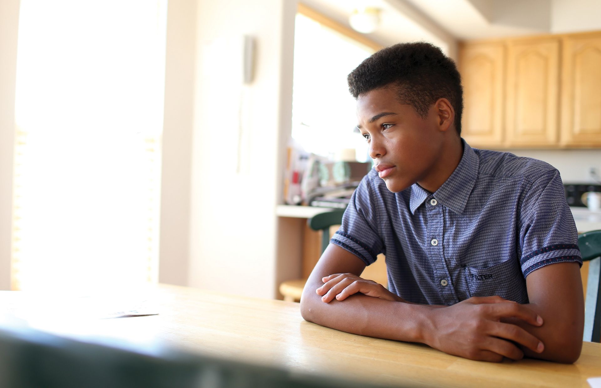 A young man pondering at a kitchen table.