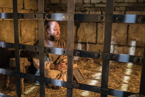 Paul, sitting in a prison cell with his hands shackled, dictating a letter to a scribe.
