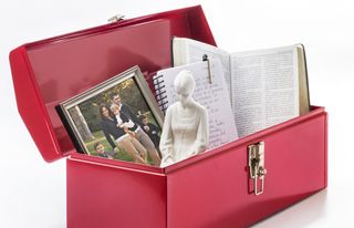 Red toolbox full of religious items including the following: scriptures, family photograph, and a woman in prayer statue,