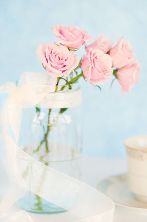 Pink roses in a jar with a ribbon tied around it on a table.