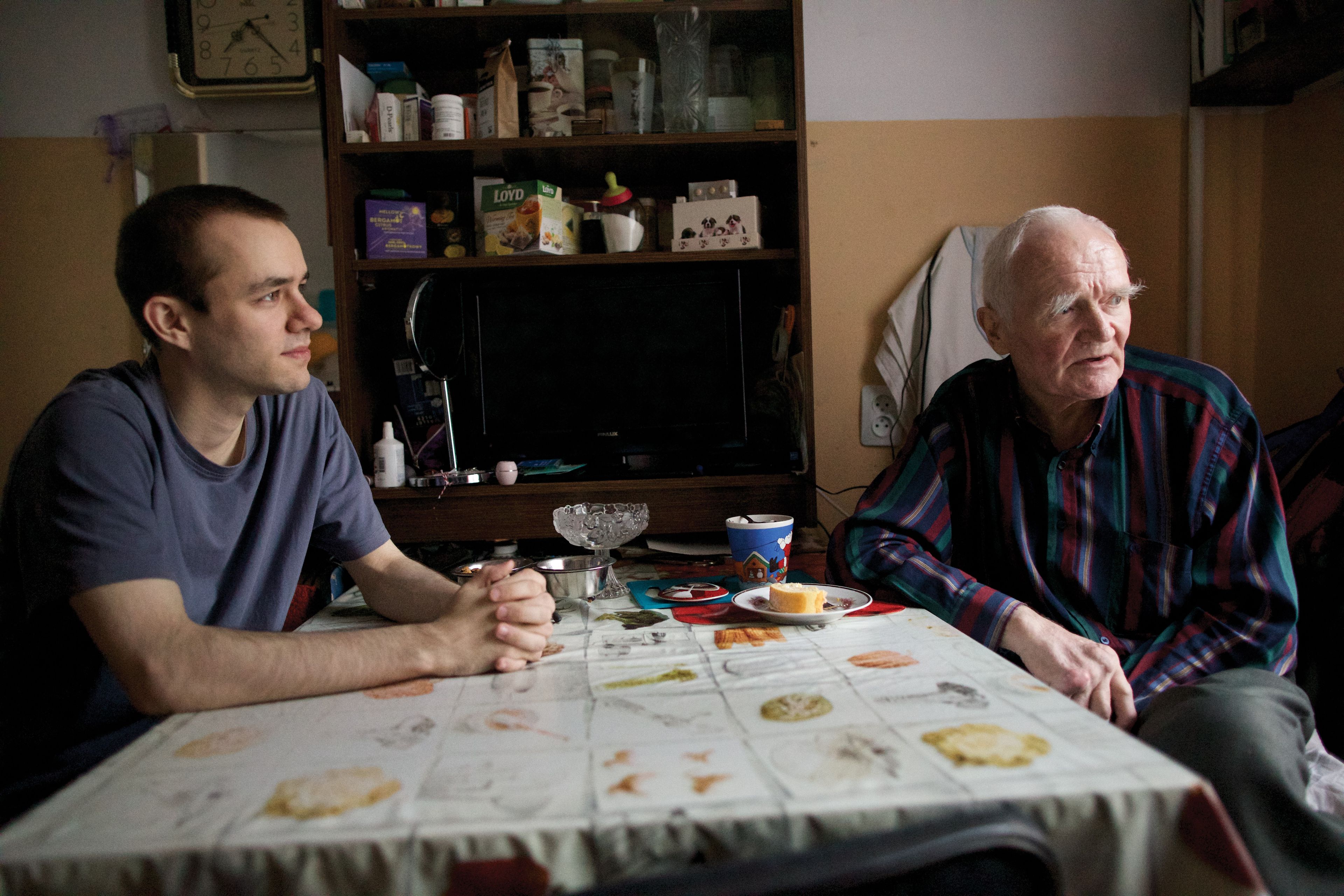A grandfather and grandson sit together at a dining table in Latvia.