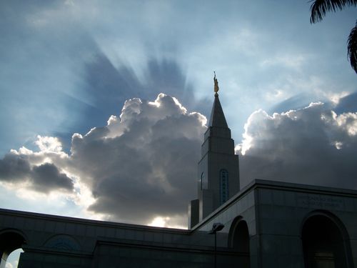 The Campinas Brazil Temple silhouetted against a bright sky, with white clouds and sunshine behind the temple spire.