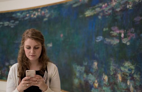 young woman looking at her phone while standing in front of a painting