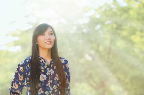 A young adult Asian woman looking slightly upward with light streaming behind her.