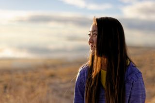 A young woman is outdoors and smiling. She is looking off to her right and away from the camera. She is at Antelope Island State Park in Utah.