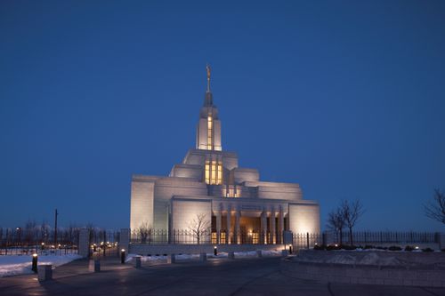A view of the entire Draper Utah Temple at night in the winter, with yellow light coming through the windows.