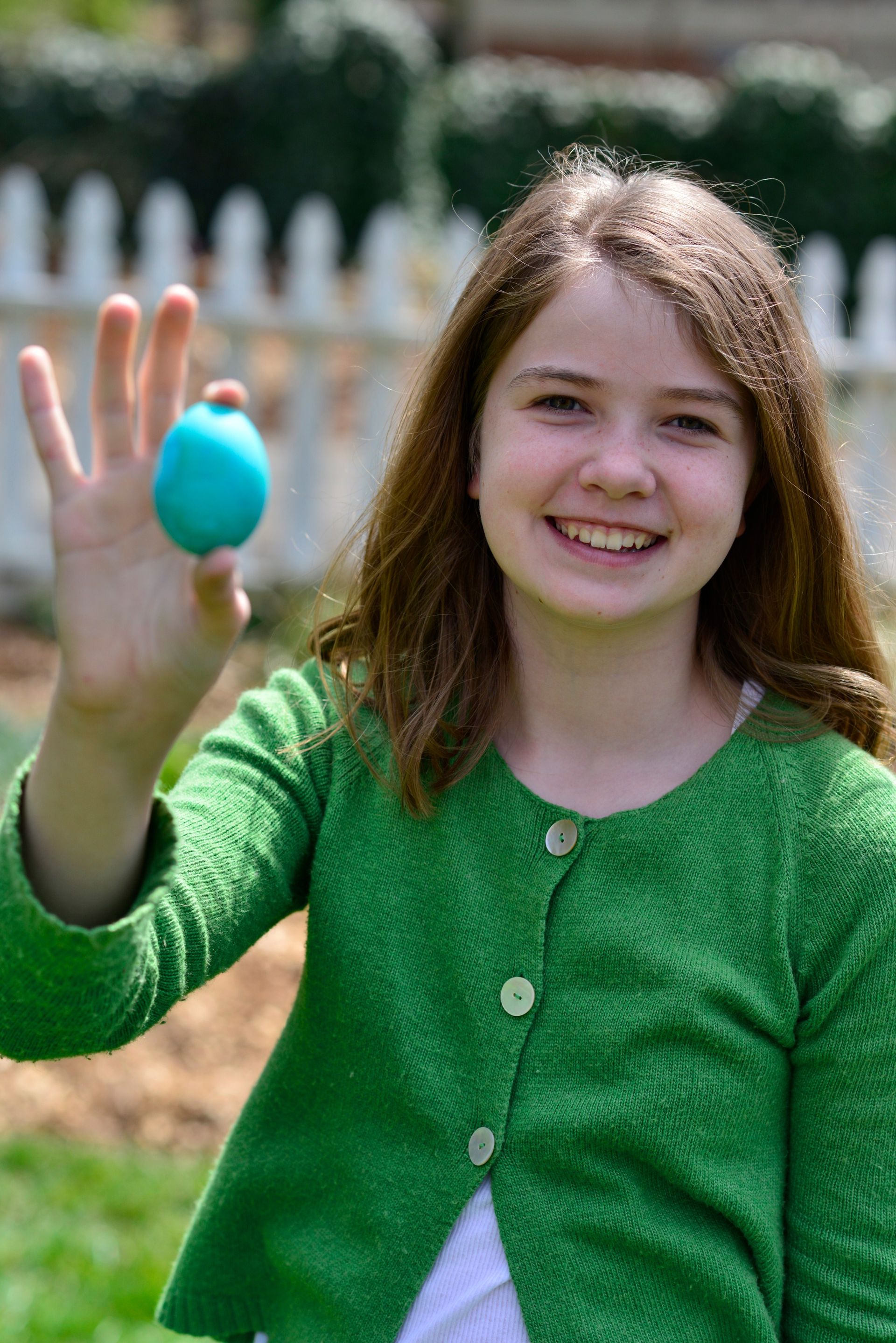 A young girl holding up a blue Easter egg outside.