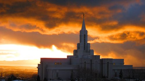 The Bountiful Utah Temple seen from afar, with a yellow and orange sunset in the background.