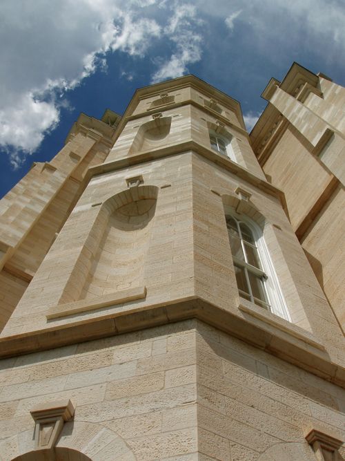 A low-angle view of part of the Manti Utah Temple exterior, including windows, with a blue sky and clouds beyond.