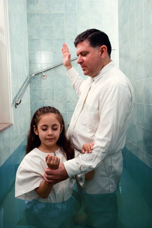 A young girl being baptized in a font by an adult man.